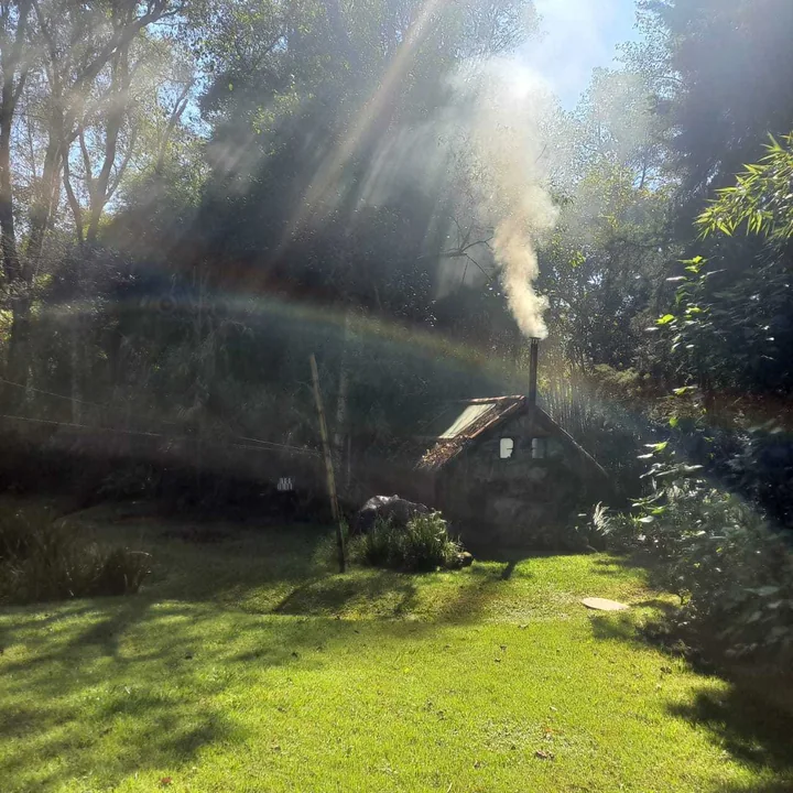 The wood-fired sauna with smoke rising from its chimney, seen across the lawn