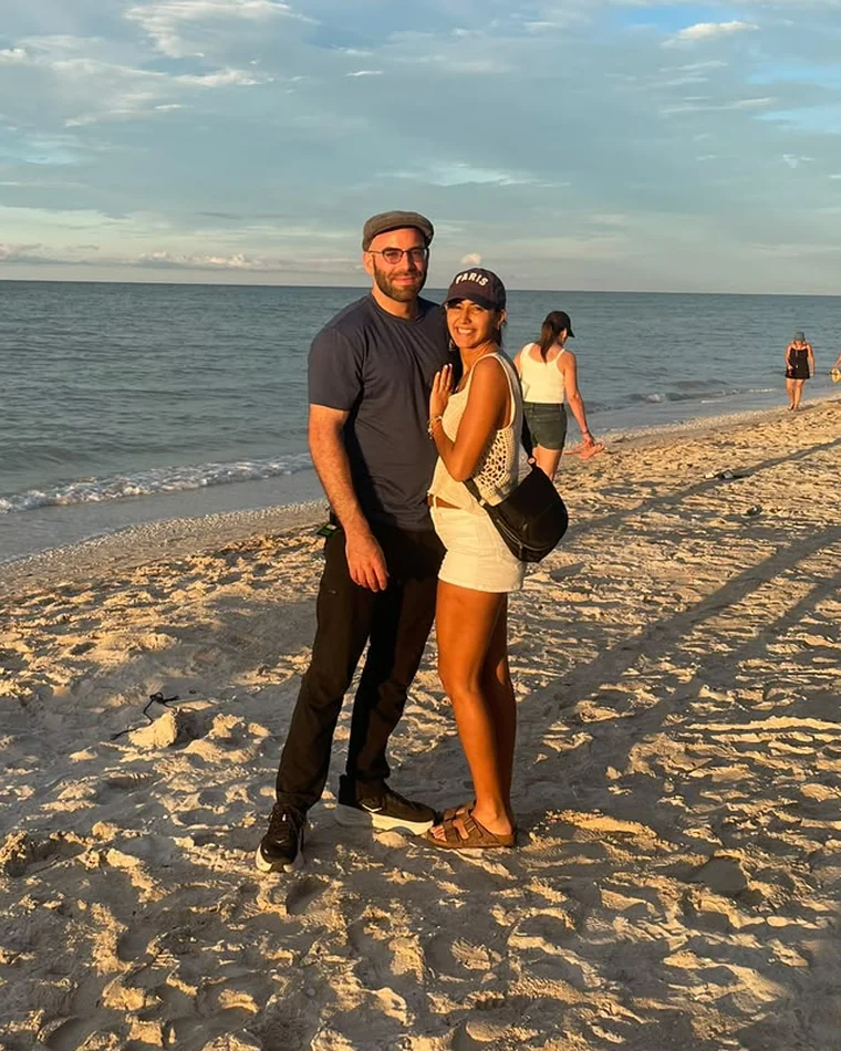 Nora and Marc standing on the sand at the edge of the water in late afternoon light